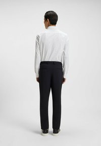 Camicia bianca a maniche lunghe con un motivo a puntini neri discreto, abbinata a pantaloni slim-fit scuri e sneakers nere. Tessuto morbido e leggero.