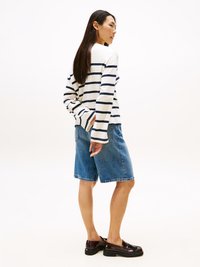 Camisola de manga longa riscada em creme e azul marinho, combinada com calções de ganga. O modelo usa sapatos estilo loafer brilhantes com sola grossa.
