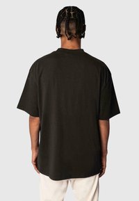 Black oversized t-shirt featuring a crew neck and short sleeves, made of cotton with a smooth texture, shown from the back.