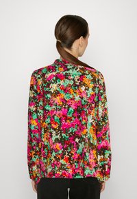 Kleurrijk shirt met bloemenpatroon, gemaakt van lichtgewicht stof. Heeft een donkere achtergrond met levendige roze, groene en oranje tinten. Lange mouwen.