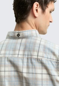 Geruite shirt met een lichtblauwe, beige en bruine kleurenschema, met een knoopdetail bij de kraag en een textuurstof.