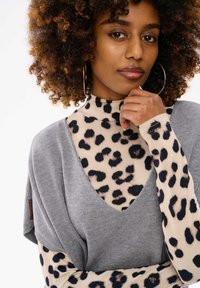 Szary sweter z głębokim dekoltem w kształcie litery V, nałożony na dopasowaną, długą bluzkę w wzór lamparta w odcieniach beżu i czerni. Wykonany z teksturowanej tkaniny.