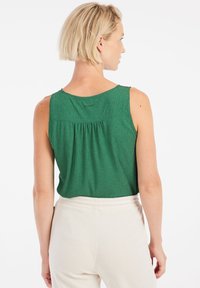 Top verde senza maniche con un motivo testurizzato e schiena arricciata. Abbinato a pantaloni in tessuto morbido di un beige chiaro.