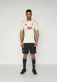 Liverpool FC hazai labdarúgó mez, krémszínű felső piros díszítéssel, fekete nadrággal és térdmagasságú zoknikon lévő csíkokkal. Az Adidas logó látható.