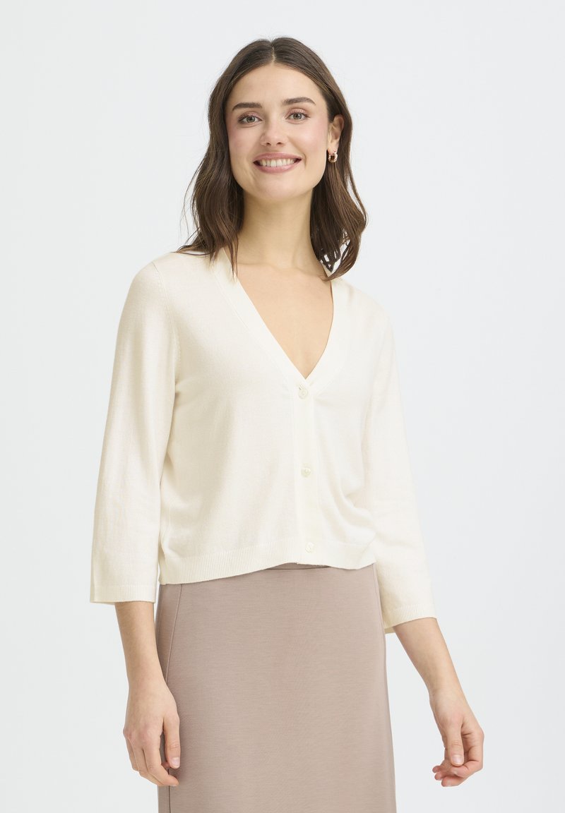 Cardigan écru court avec un col en V, manches trois-quarts, et cinq boutons, confectionné dans un tissu en maille douce.