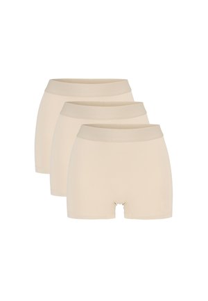 Tre beige, sømløse boyshort-underbukser stablet diagonalt på en hvid baggrund.