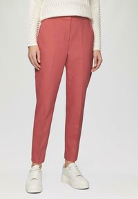 Stofrose getailleerde broeken met voorplooien, gecombineerd met chunky witte sneakers. Gebreide witte top voegt textuur en contrast toe.