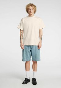 Kreemjas puuvillane T-särk lühikeste varrukatega, mugava lõikega; kokku sobitatud hele siniste teksapükstega, valgete sokkide ja mustade libisevate kingadega.