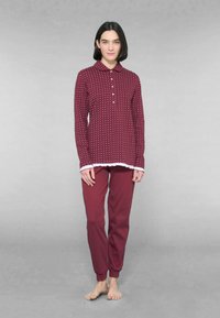 Set di pigiama bordeaux con top a maniche lunghe con bottoni, dotato di colletto e dettagli bianchi, abbinato a pantaloni tapered coordinati. Texture liscia.