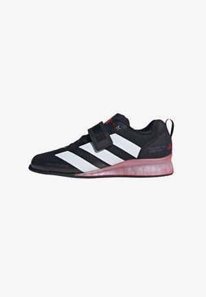 Black athletic shoes with white stripes, textured mesh upper, adjustable strap, and pink-tinted translucent sole. Logo on heel.