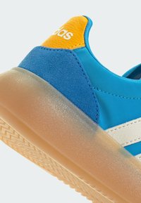 Plava tenisica s gornjim dijelom od brušene kože i sintetičkog materijala, bijelim prugama i teksturiranim narančastim detaljem. Ima prozirni gumeni potplat.