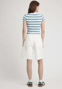 Short en denim blanc avec une coupe décontractée et deux poches arrière, associé à un haut à manches courtes rayé en blanc, vert et bleu.