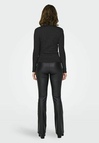 Top a maniche lunghe nero a coste con orlo scalloped, abbinato a pantaloni attillati in ecopelle nera. Modella di spalle rispetto alla macchina fotografica.