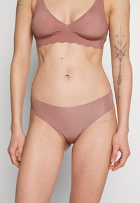 Light rose-colored bra with a scalloped edge and matching seamless briefs. The fabric is smooth, offering a minimalistic design.