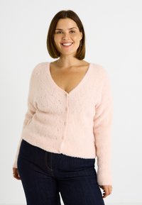 Cardigan tricoté rose clair avec un col en V, présentant un motif texturé, des manches longues et six boutons sur le devant. Matière douce et duveteuse.