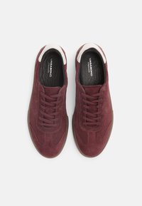 Burgundy suede sneakers with a smooth white leather accent at the collar, featuring brown rubber soles and traditional lace-up design.