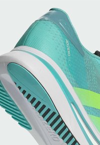 Scarpa da corsa aqua con tomaia in rete, dettagli testurizzati e accenti gialli vivaci. Presenta una suola bianca imbottita con motivi di trazione.
