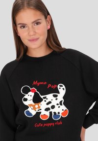 Fekete pulóver, színes, bolyhos kutyadeszínnel, pöttyökkel, piros szöveggel: "Mymo Pop" és "Cute puppy club", valamint kontrasztos színű díszítésekkel.