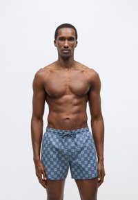 Blauwe zwemshorts met patroon, voorzien van een elastische tailleband en trekkoord. Heeft een herhaald logo-ontwerp. Lichtgewicht stof, mid-dij lengte.