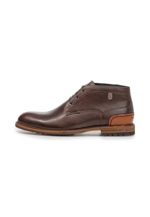 Stivaletto alla caviglia in pelle marrone scuro con chiusura frontale con lacci e toppa sul tallone color tan a contrasto, mostrato su uno sfondo bianco.