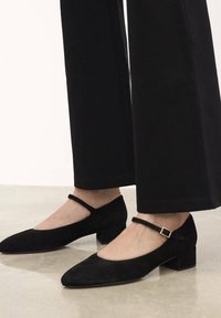 Scarpe Mary Jane in suede nero con punta affilata, tacco basso a blocco e una cinghia alla caviglia regolabile con una piccola fibbia in metallo.