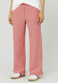 Un pantalon à carreaux rouge et blanc, de coupe ample, avec un ourlet effiloché et une taille élastique, associé à des baskets blanches.