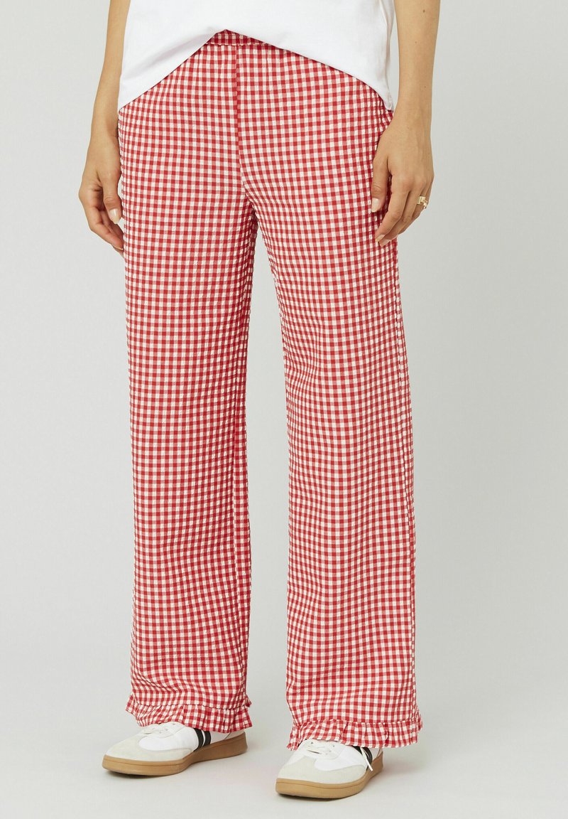 Un pantalon à carreaux rouge et blanc, de coupe ample, avec un ourlet effiloché et une taille élastique, associé à des baskets blanches.