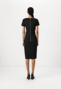 Black fitted dress with short sleeves, side seam pockets, and a back zipper detail. Knee-length with a smooth, structured texture.