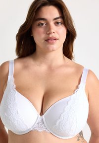 Witte bh met kant aan de rand en een diep decolleté, zachte gevoerde cups en verstelbare bandjes. Heeft bloemenkant accenten aan de zijkanten.