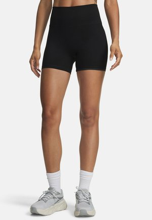 Woman wearing black high-waist athletic shorts, white socks, and light gray running shoes standing against a plain background.