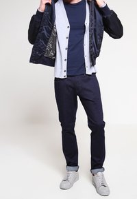 Námořnická bombardérka s šedým interiérem, šedý kardigan na knoflíky pod ní, námořnická košile, tmavé džíny a šedé tenisky.