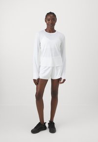White long-sleeve athletic top and matching shorts, made of lightweight fabric. Features a rounded neckline and minimalist design. Black sneakers.