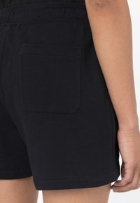 Pantalones cortos de algodón negros con un bolsillo trasero plano, cinturilla elástica y dobladillo curvado. La tela parece suave y ligeramente elástica.