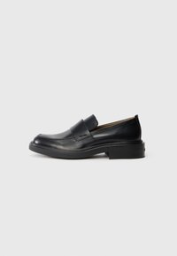 Pantofle negre din piele pentru bărbați, cu toc mic și un logo subtil Calvin Klein pe lateral, prezentate în profil pe un fond alb.