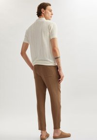 Gebreide polo in off-white met verticale ribbels, gecombineerd met bruine textuur broek en instap schoenen. Achteraanzicht toont het ontwerpdetails.