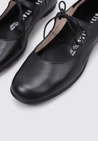 Bailarinas de cuero negro con un acabado texturizado, que cuentan con un diseño de punta redonda y una suela plana, aseguradas con delgados cordones a lo largo del empeine.