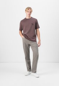 T-shirt court marron à manches courtes avec un petit graphique noir. Assorti à un pantalon en velours côtelé gris clair et des baskets blanches. Ensemble simple et décontracté.