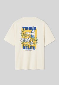 T-shirt beige avec un motif carré jaune montrant une bouteille de vin, deux verres, des boules de pétanque, des feuilles vertes et le texte bleu "TIREUR DELITE."