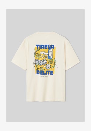 T-shirt beige avec un motif carré jaune montrant une bouteille de vin, deux verres, des boules de pétanque, des feuilles vertes et le texte bleu "TIREUR DELITE."