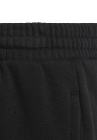 Närbild av svart tyg med elastisk midja och synlig ficksöm på lätta stickade byxor eller shorts.