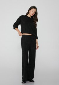 Zwarte kabelgebreide trui met een relaxed fit en een cropped zoom, gecombineerd met bijpassende wijde broek. Soepele textuur, minimale details, casual ontwerp.