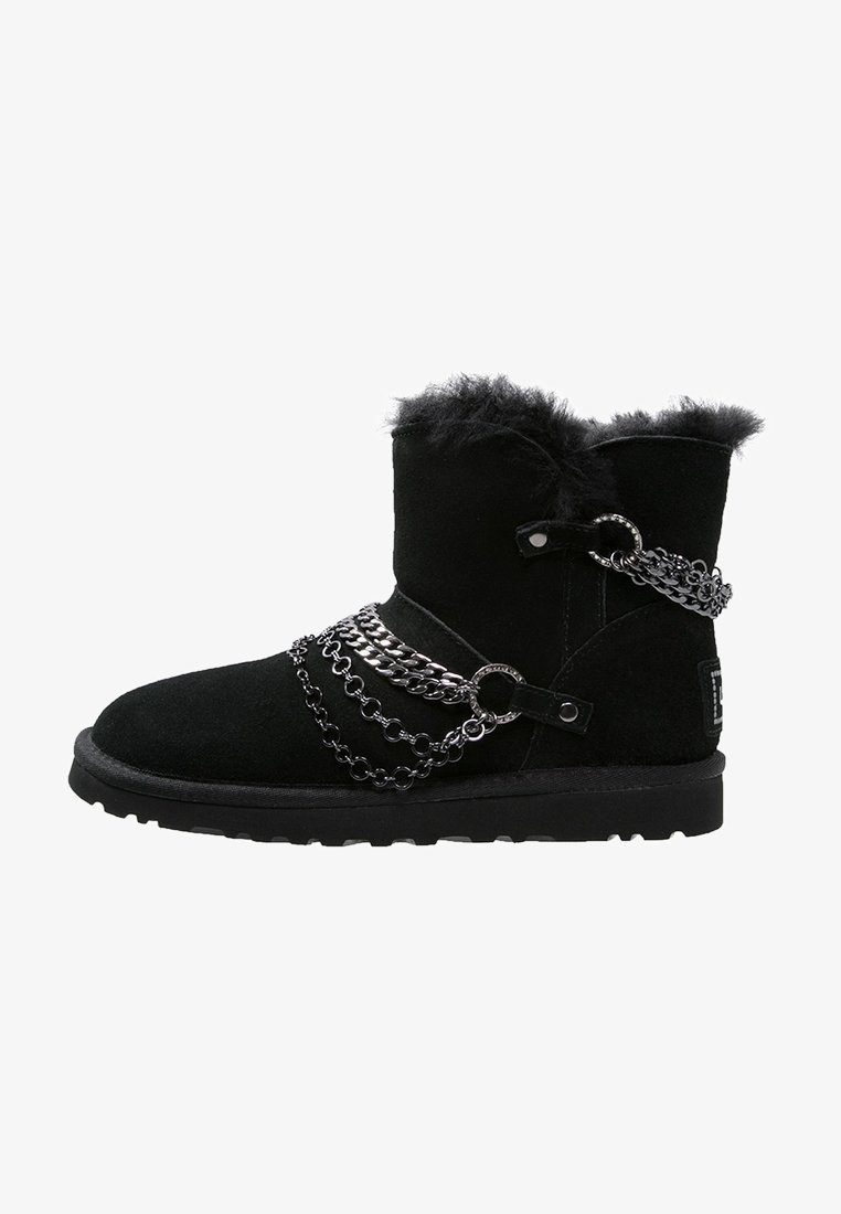 Bottine en daim noir avec doublure duveteuse et chaînes argentées décoratives entourant la tige et la zone du pied.