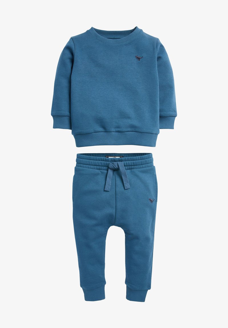 Sweatshirt bleu et pantalon assorti, fabriqués en tissu doux avec des poignets et une taille côtelés ; comporte un petit emblème sur la poitrine et la jambe.