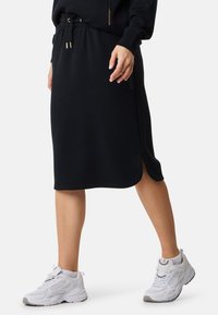 Zwarte jurk rok met een trekkoord in de taille, zijsplits en logo-accenten, gecombineerd met witte sportschoenen. Gladde textuur en casual ontwerp.