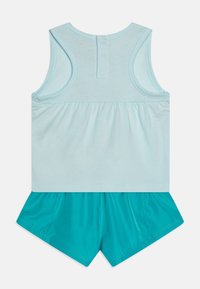 Top senza maniche blu chiaro con vita arricciata, abbinato a pantaloni corti turchesi lucidi con taglio a campana.