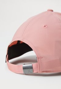 Lyserød baseballcap med tekstureret stof, buet skygge og justerbar rem med et metallisk logo-akkent.