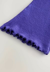 Lila strukturierter Stoff mit einem welligen, gefransten Rand, der eine gemusterte Oberfläche und ein weiches, gestricktes Aussehen aufweist.