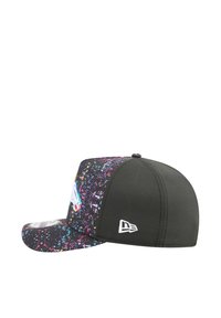La casquette présente une base noire avec un motif de éclaboussures colorées. Design structuré avec une visière incurvée et un logo brodé sur le côté.