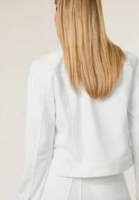 Weiße Jeansjacke mit einem verkürzten Design, geradem Rücken, strukturierten Schultern und Nähdetails. Glatte Textur.