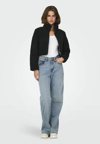 Zwarte cropped jack in pluche stof met een hoge kraag, gecombineerd met lichtblauwe high-waisted jeans en witte sneakers.